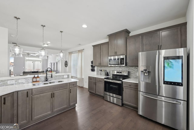 kitchen featuring stainless steel appliances, light countertops, decorative backsplash, dark wood-type flooring, and a sink