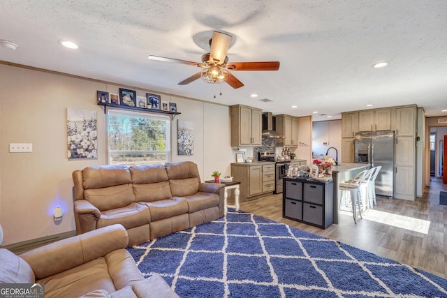 living room with ceiling fan, sink, light hardwood / wood-style floors, and a textured ceiling