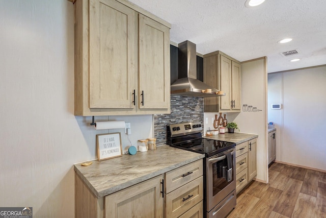 kitchen featuring a textured ceiling, stainless steel electric stove, light hardwood / wood-style floors, decorative backsplash, and wall chimney range hood