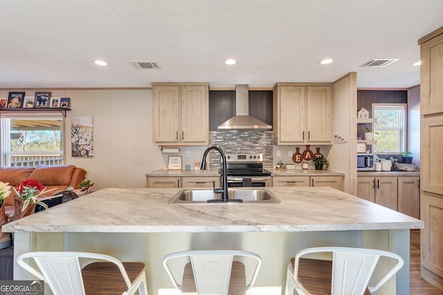 kitchen featuring a kitchen breakfast bar, sink, light brown cabinets, and wall chimney range hood