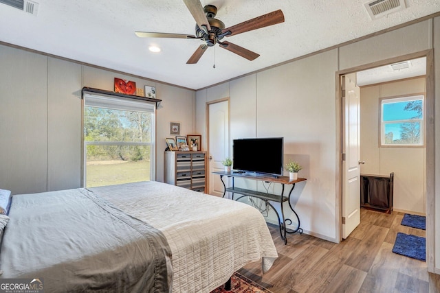 bedroom with ceiling fan, light hardwood / wood-style floors, crown molding, a textured ceiling, and ensuite bath