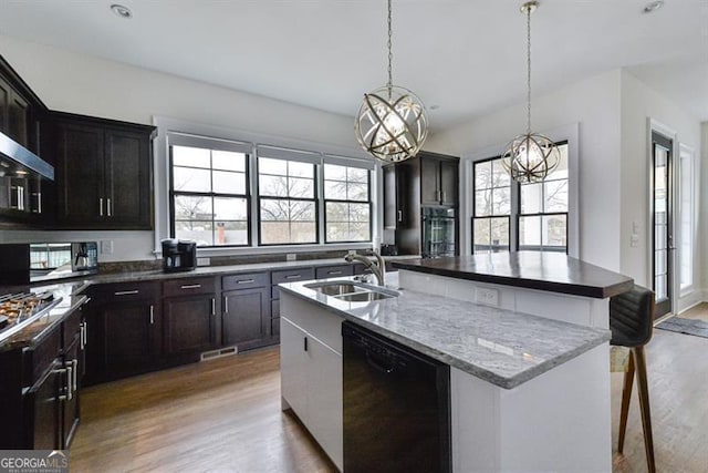 kitchen featuring a breakfast bar, black dishwasher, sink, hardwood / wood-style flooring, and a kitchen island with sink