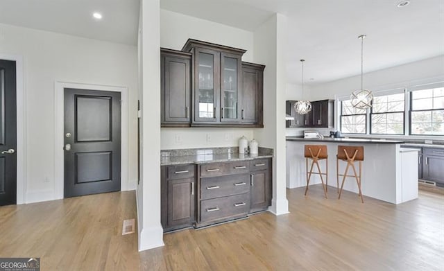 kitchen featuring decorative light fixtures, a kitchen bar, dark stone counters, dark brown cabinetry, and light hardwood / wood-style flooring