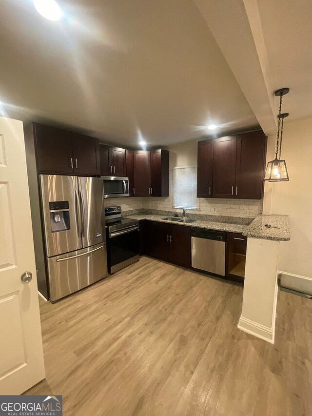 kitchen with sink, light stone counters, decorative light fixtures, appliances with stainless steel finishes, and light hardwood / wood-style floors