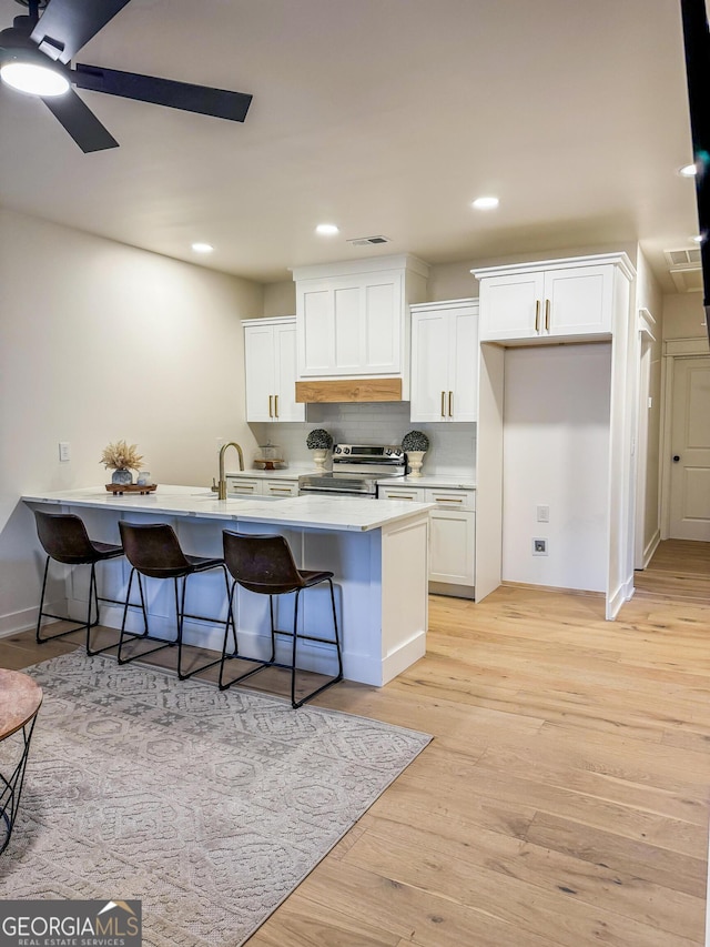 kitchen with a breakfast bar, white cabinets, light hardwood / wood-style floors, and stainless steel electric range