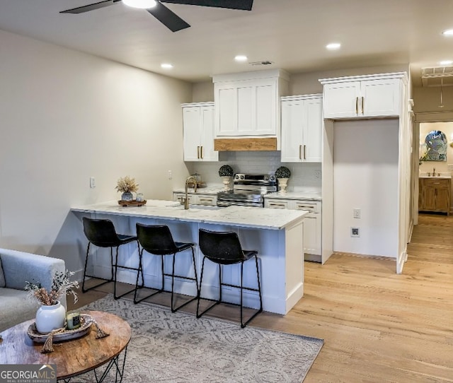 kitchen featuring light wood-type flooring, white cabinets, a kitchen breakfast bar, and stainless steel range with electric stovetop