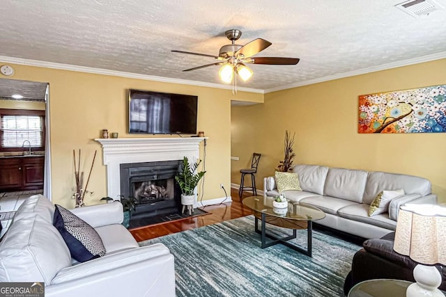 living room featuring sink, hardwood / wood-style flooring, ornamental molding, ceiling fan, and a textured ceiling