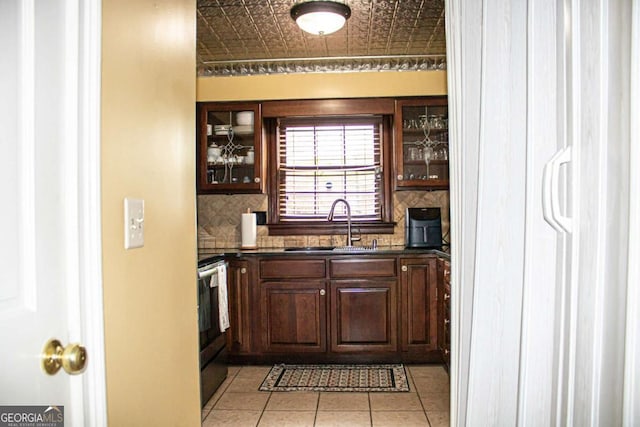 bar with dark brown cabinetry, sink, light tile patterned floors, electric range, and backsplash