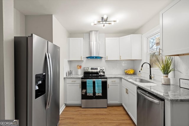 kitchen featuring appliances with stainless steel finishes, sink, white cabinets, light stone counters, and wall chimney exhaust hood