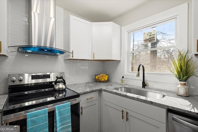 kitchen with appliances with stainless steel finishes, sink, white cabinets, light stone countertops, and wall chimney range hood