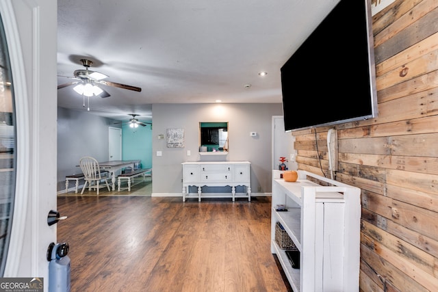 living room with dark hardwood / wood-style flooring, ceiling fan, and wood walls