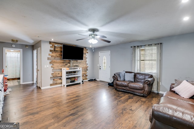 living room featuring dark wood-type flooring, ceiling fan, and a textured ceiling