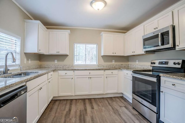 kitchen with sink, appliances with stainless steel finishes, white cabinetry, ornamental molding, and light stone countertops