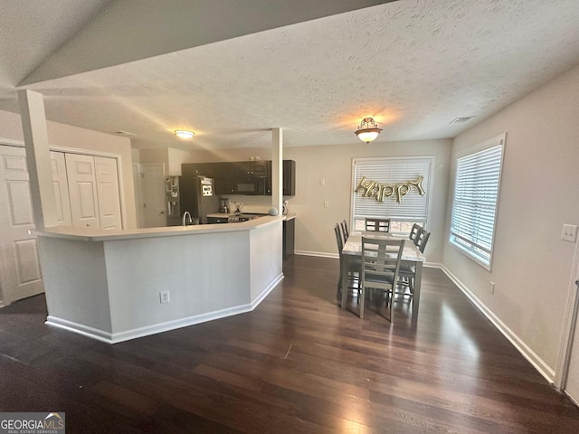 kitchen featuring dark wood-type flooring, a center island with sink, a textured ceiling, and stainless steel refrigerator with ice dispenser