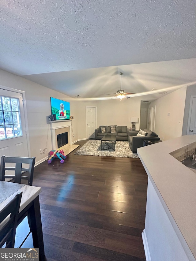 living room with ceiling fan, vaulted ceiling, a textured ceiling, and dark hardwood / wood-style flooring