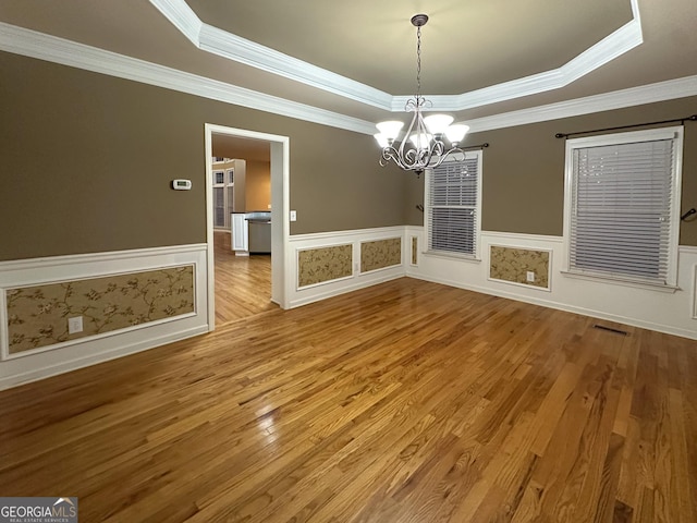 unfurnished dining area featuring crown molding, a tray ceiling, wood-type flooring, and a chandelier