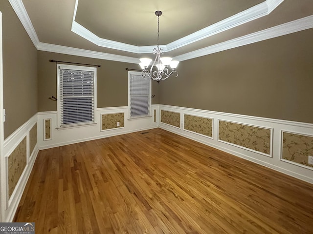 empty room featuring crown molding, hardwood / wood-style floors, an inviting chandelier, and a tray ceiling