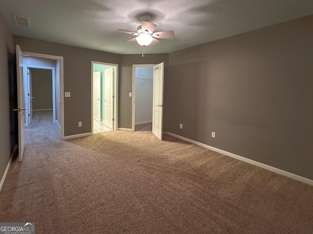 unfurnished bedroom with ceiling fan, a walk in closet, light colored carpet, and a closet