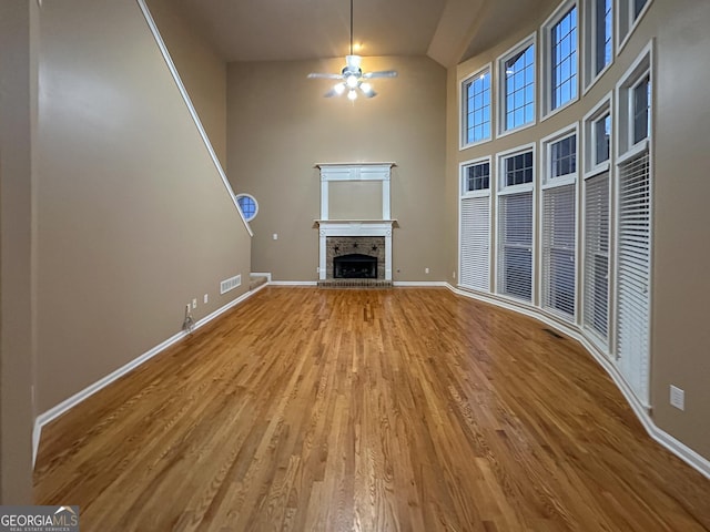 unfurnished living room with hardwood / wood-style flooring, ceiling fan, and a high ceiling