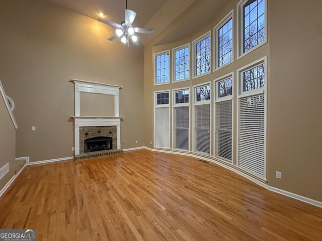 unfurnished living room with ceiling fan, a towering ceiling, light hardwood / wood-style floors, and a brick fireplace