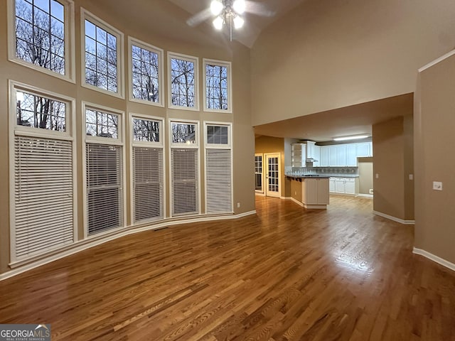 unfurnished living room featuring ceiling fan, wood-type flooring, and a high ceiling