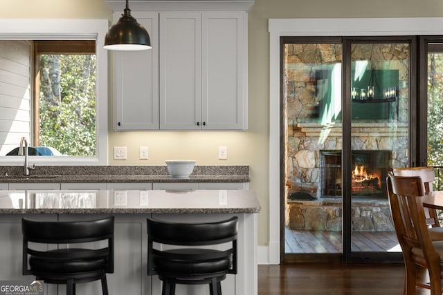 bar featuring white cabinetry, sink, pendant lighting, and dark stone counters