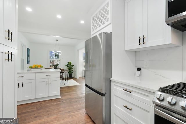 kitchen with appliances with stainless steel finishes, light stone counters, white cabinets, hanging light fixtures, and tasteful backsplash