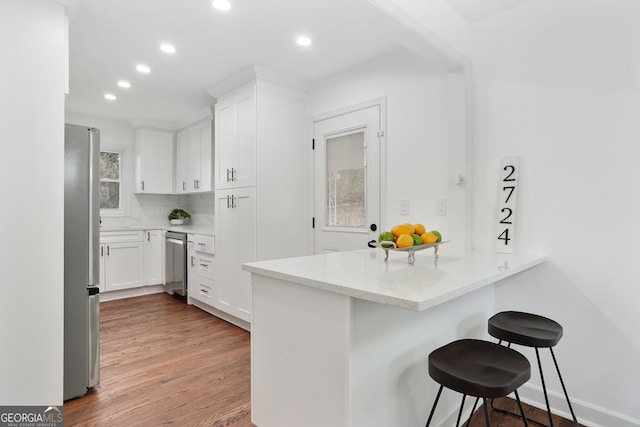 kitchen with white cabinetry, kitchen peninsula, a breakfast bar, light stone counters, and appliances with stainless steel finishes