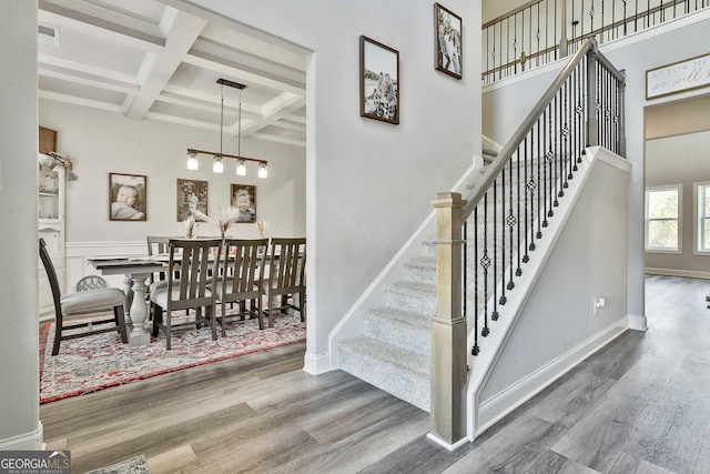 staircase featuring beamed ceiling, wood-type flooring, coffered ceiling, and a chandelier