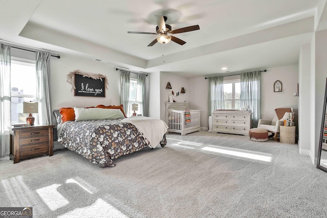 carpeted bedroom with multiple windows, a tray ceiling, and ceiling fan