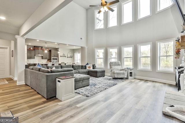 living room featuring ceiling fan, a towering ceiling, decorative columns, and light wood-type flooring