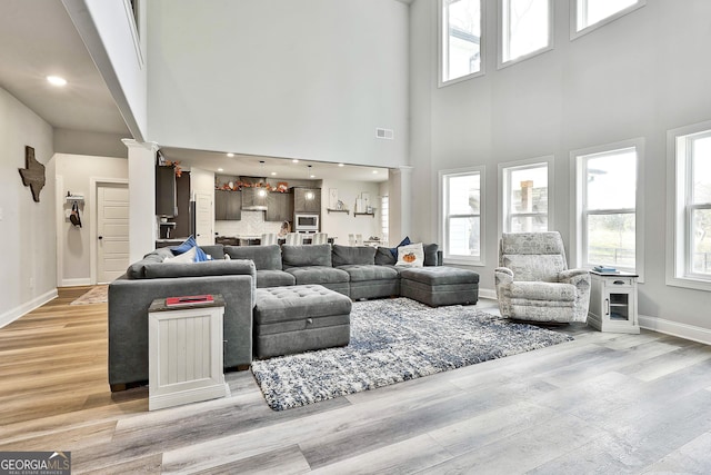 living room with a towering ceiling, decorative columns, and light hardwood / wood-style floors