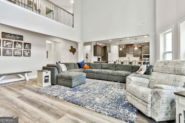 living room with sink, decorative columns, light hardwood / wood-style floors, and a high ceiling