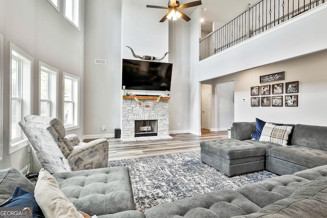 living room with ceiling fan, a towering ceiling, a stone fireplace, and hardwood / wood-style floors