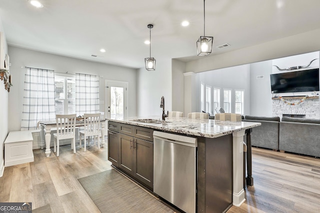 kitchen featuring sink, hanging light fixtures, stainless steel dishwasher, an island with sink, and light stone countertops