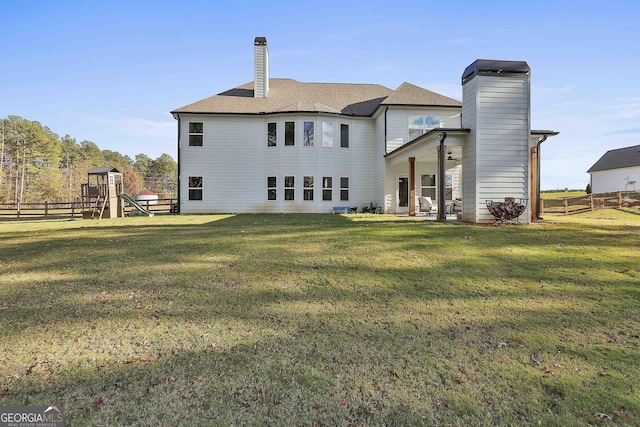 rear view of house with ceiling fan, a lawn, and a playground