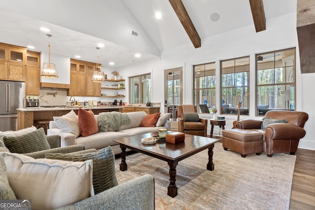 living area with high vaulted ceiling, a wealth of natural light, beam ceiling, and light wood-style floors