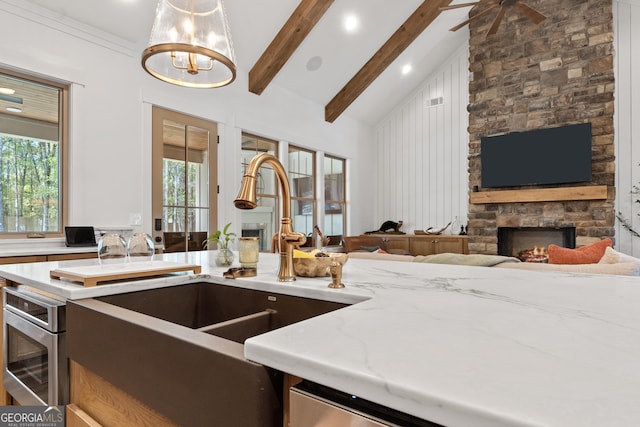 kitchen with a sink, open floor plan, beam ceiling, and a stone fireplace