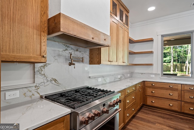 kitchen featuring custom exhaust hood, stainless steel stove, glass insert cabinets, brown cabinetry, and light stone countertops