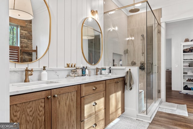 full bathroom with double vanity, ornamental molding, a stall shower, a sink, and wood finished floors