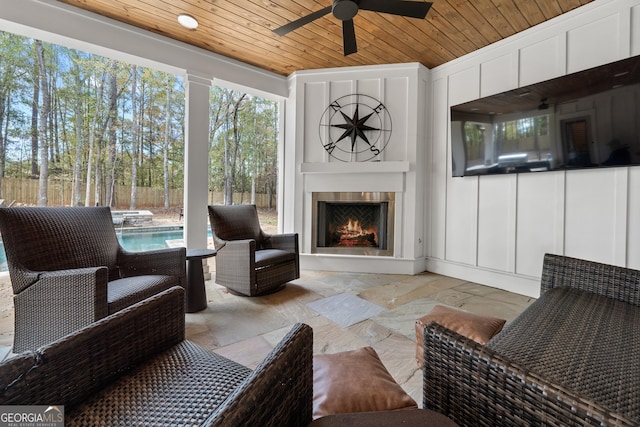 sunroom / solarium with a ceiling fan, a warm lit fireplace, and wood ceiling