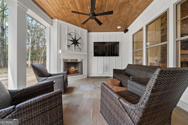 sunroom featuring a ceiling fan, wooden ceiling, and a lit fireplace