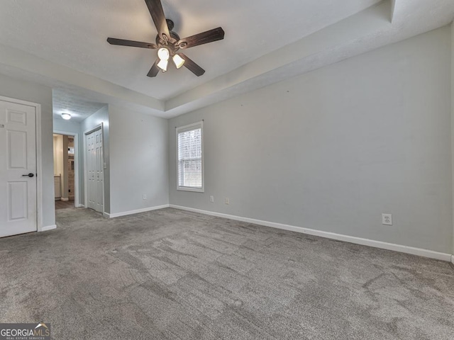 empty room featuring ceiling fan, a tray ceiling, and carpet