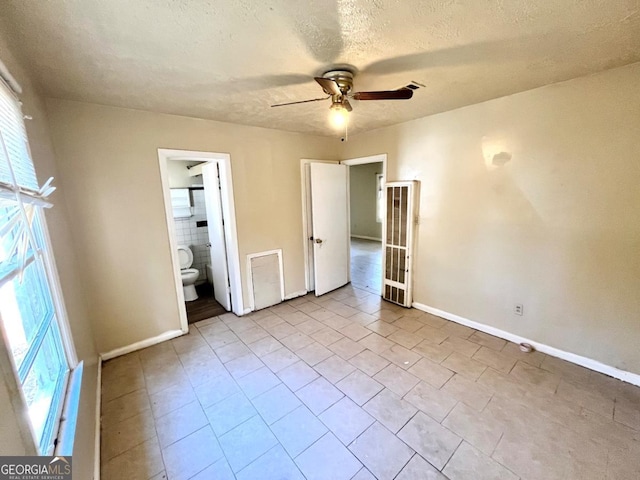 unfurnished bedroom featuring ceiling fan, light tile patterned floors, a textured ceiling, and ensuite bath