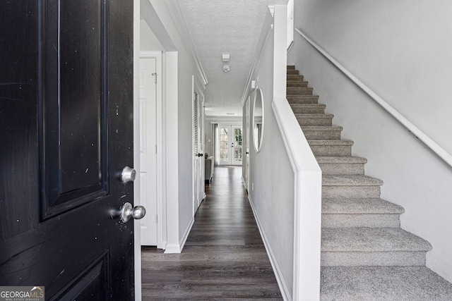 entryway with dark wood-type flooring, ornamental molding, and a textured ceiling