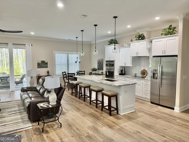 kitchen with pendant lighting, appliances with stainless steel finishes, a kitchen island with sink, and white cabinets