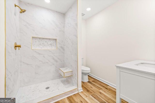 bathroom featuring a tile shower, vanity, wood-type flooring, and toilet