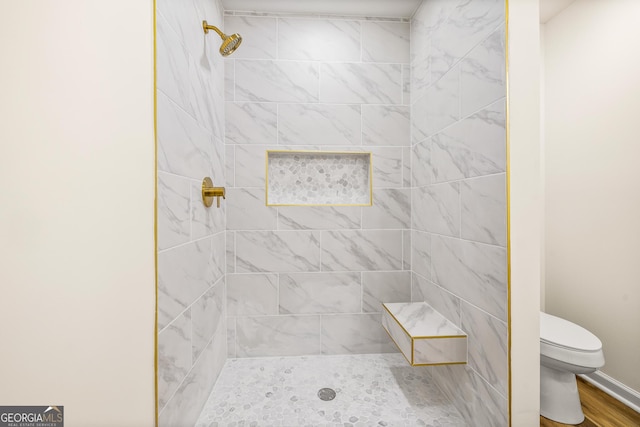 bathroom featuring hardwood / wood-style flooring, toilet, and a tile shower