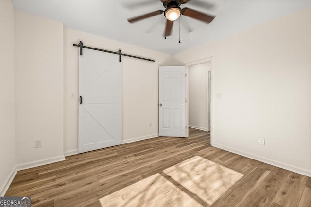 unfurnished bedroom featuring hardwood / wood-style flooring, a barn door, and ceiling fan