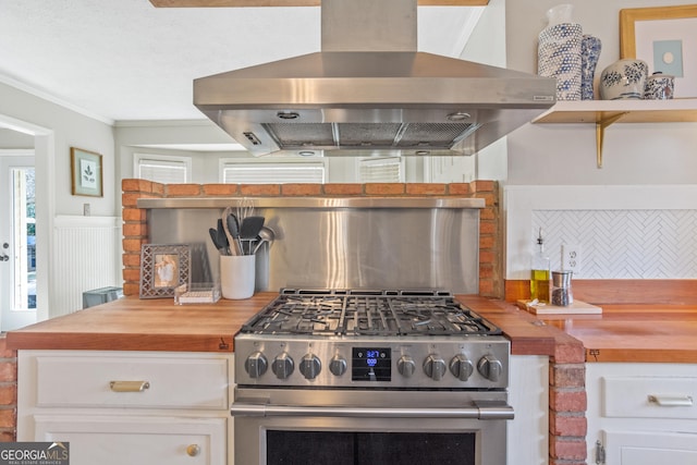 kitchen with island range hood, butcher block countertops, backsplash, white cabinets, and stainless steel range with gas stovetop